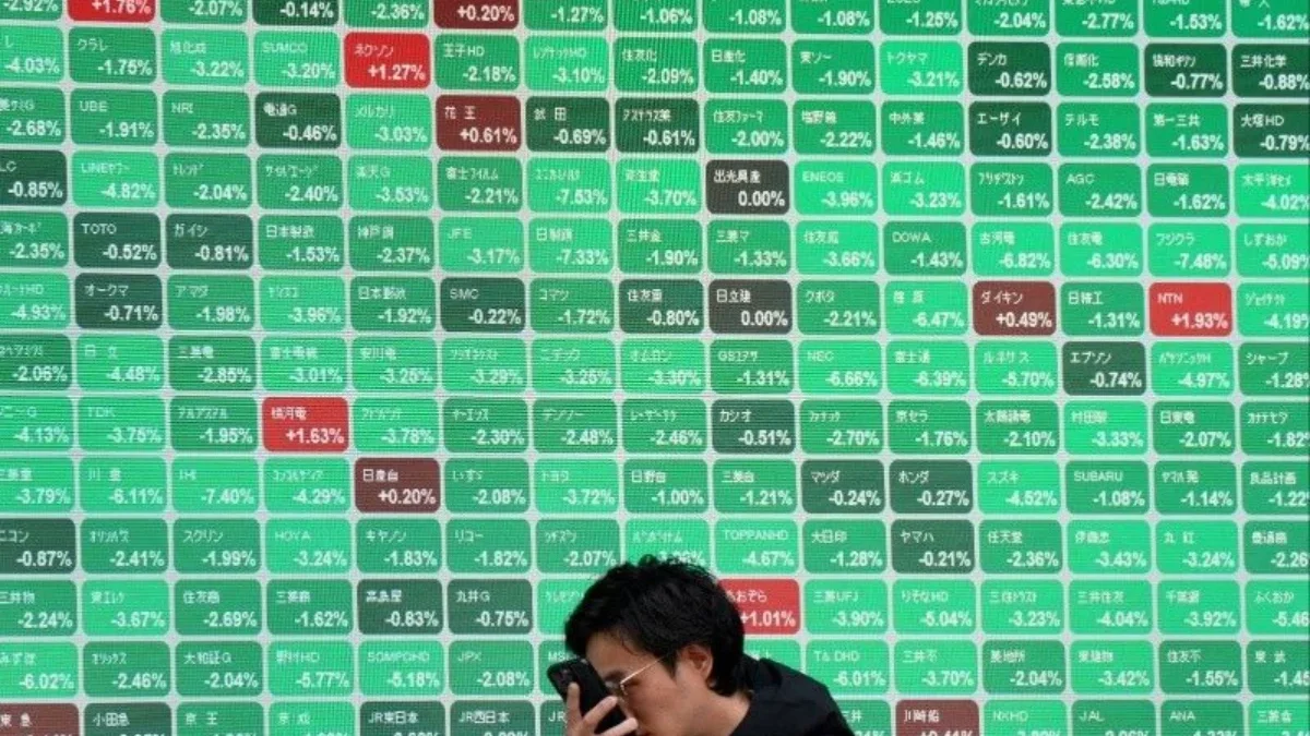 Seorang pria berjalan melewati papan elektronik yang menunjukkan indeks Nikkei 225 di Bursa Efek Tokyo di sepa