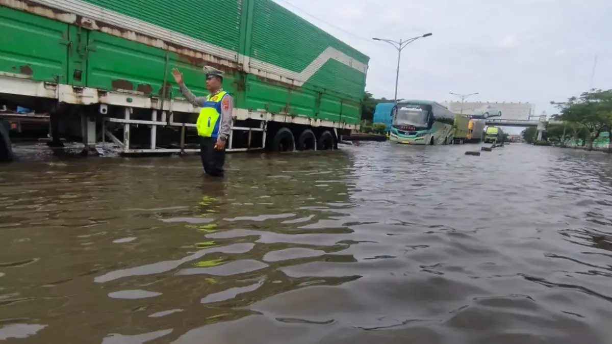 Petugas tengah mengatur kendaraan di ruas jalan yang masih tergenang air. (Ist)