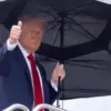 Presiden Amerika Serikat Donald Trump mengacungkan jempol sambil membawa payung saat akan menaiki pesawat kepr