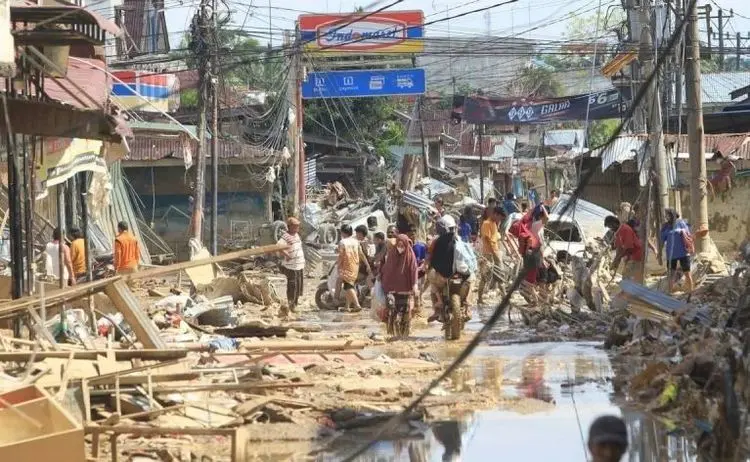 Warga melintasi material arus banjir di kawasan Desa Bukit Tempurung, Kota Kuala Simpang, Kabupaten Aceh Tamia