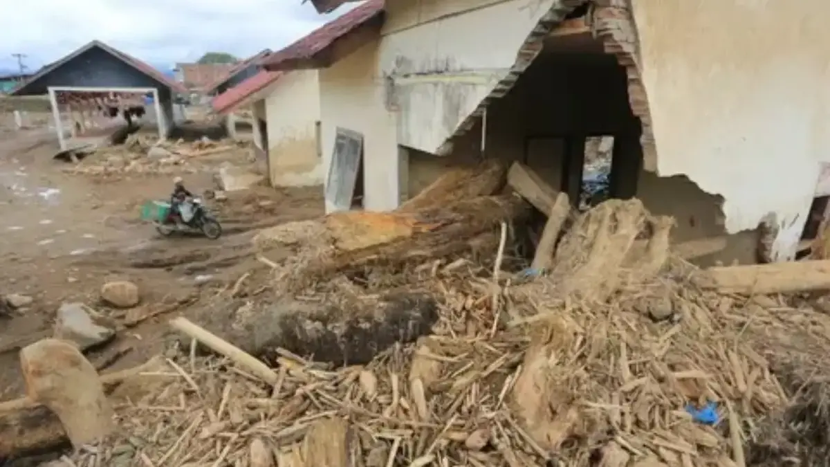 Pengendara sepeda motor melintas di dekat rumah yang rusak parah akibat banjir bandang di Desa Buntul Kemumu,