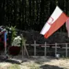 Seorang pria yang memegang bendera nasional Polandia di lokasi upacara pemakaman massal orang Polandia yang di