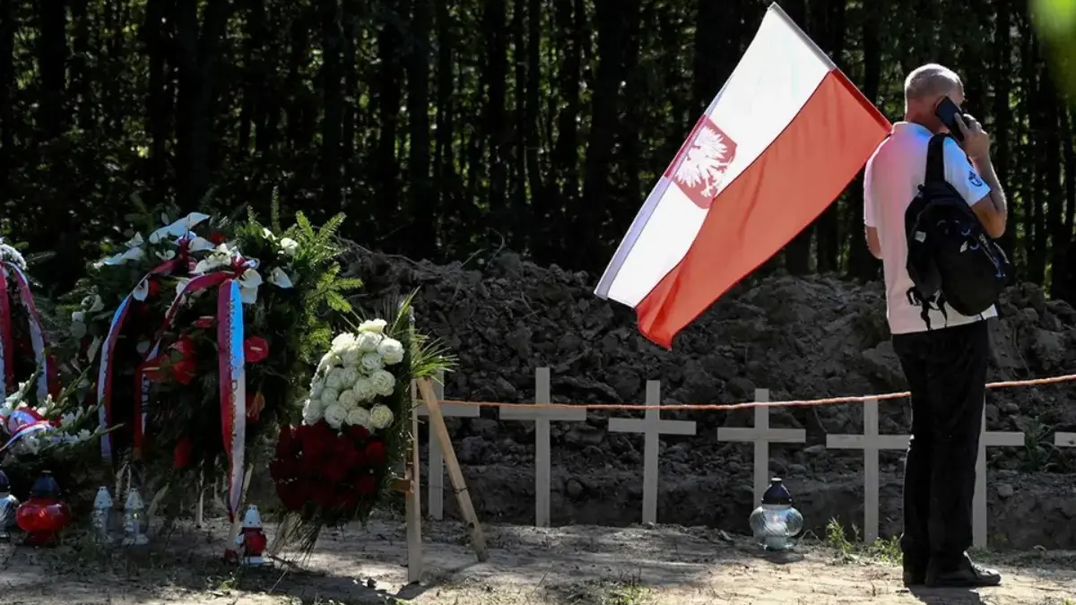 Seorang pria yang memegang bendera nasional Polandia di lokasi upacara pemakaman massal orang Polandia yang di